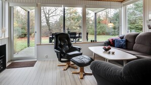 A modern interior with a wooden ceiling, large windows, a leather chair, a sofa, and a small table.