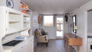 Une pièce avec un plancher en bois, une armoire blanche avec des tiroirs, une chaise, une petite table et une fenêtre avec des rideaux.