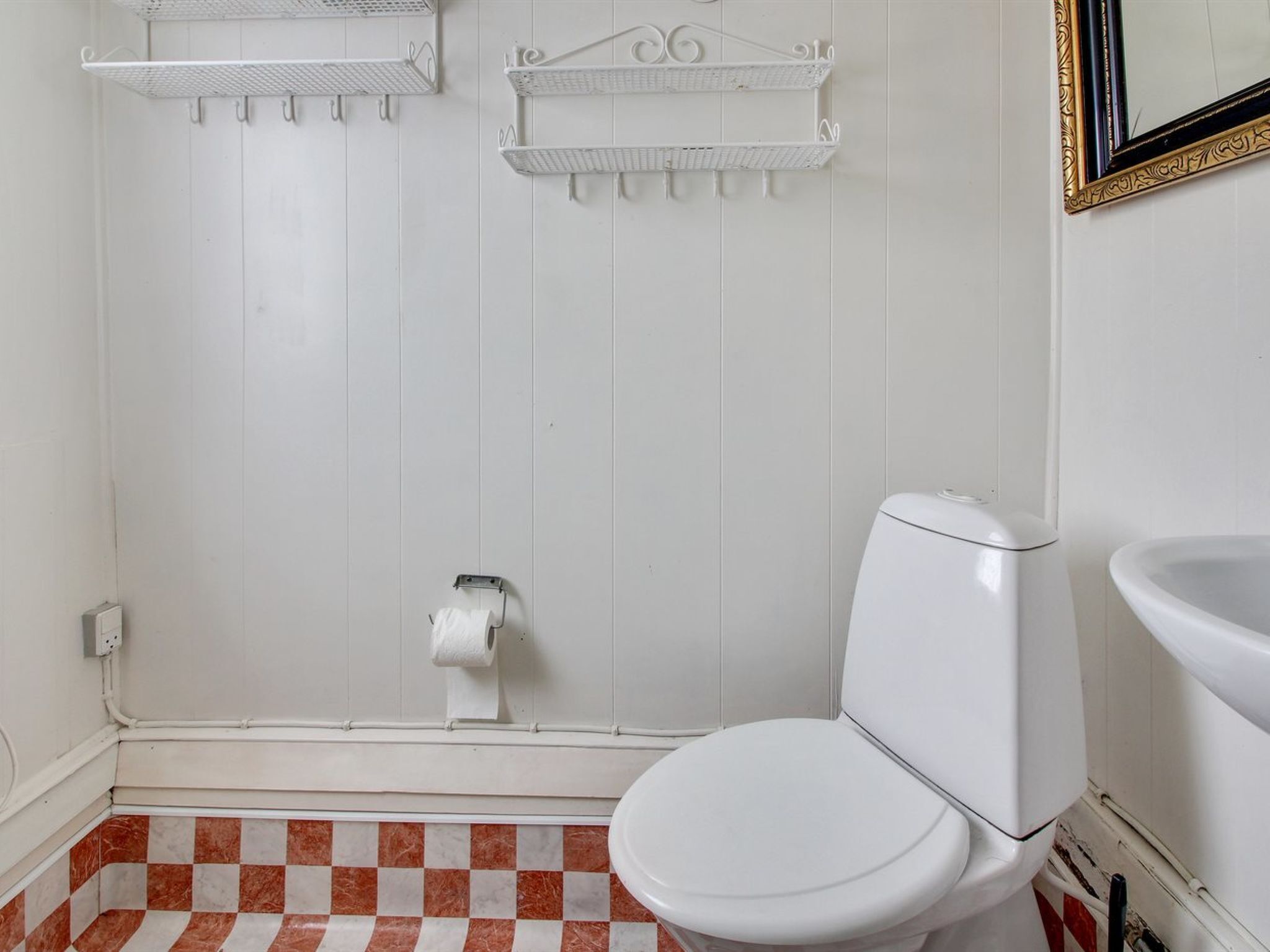 A bathroom with a toilet, a roll of toilet paper, and a shower area with a metal shelf.