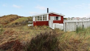 Un petit bâtiment rouge avec un toit blanc, portant le numéro 66, situé sur une colline herbeuse, non loin d’une clôture en bois.