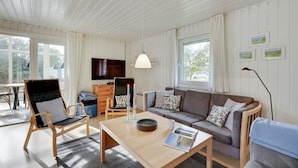 Een ruime woonkamer met een bank, fauteuils, een salontafel en een televisie.