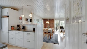 Een moderne keuken met witte kastjes, een eethoek met houten stoelen en een accentmuur van baksteen.