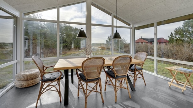 Ruime kamer met een grote tafel en rieten stoelen, grote ramen met uitzicht op de omgeving, en hanglampen.