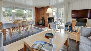 Een gezellige woonkamer met een open haard, houten meubels en een groot raam met uitzicht op groen.