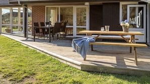 Een overdekt terras met een houten tafel en stoelen, een bank en een bakstenen schoorsteen.