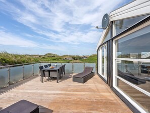 A deck with a table and chairs, a lounge chair, and a glass railing overlooking a landscape with hills and a body of water. - "Swerting" - 230m from the sea by Interhome (Saltum)