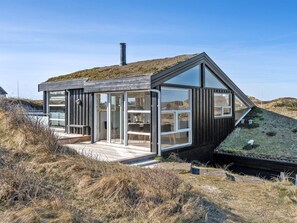 Une maison moderne avec un toit en pente, de grandes fenêtres en verre et une terrasse en bois.
