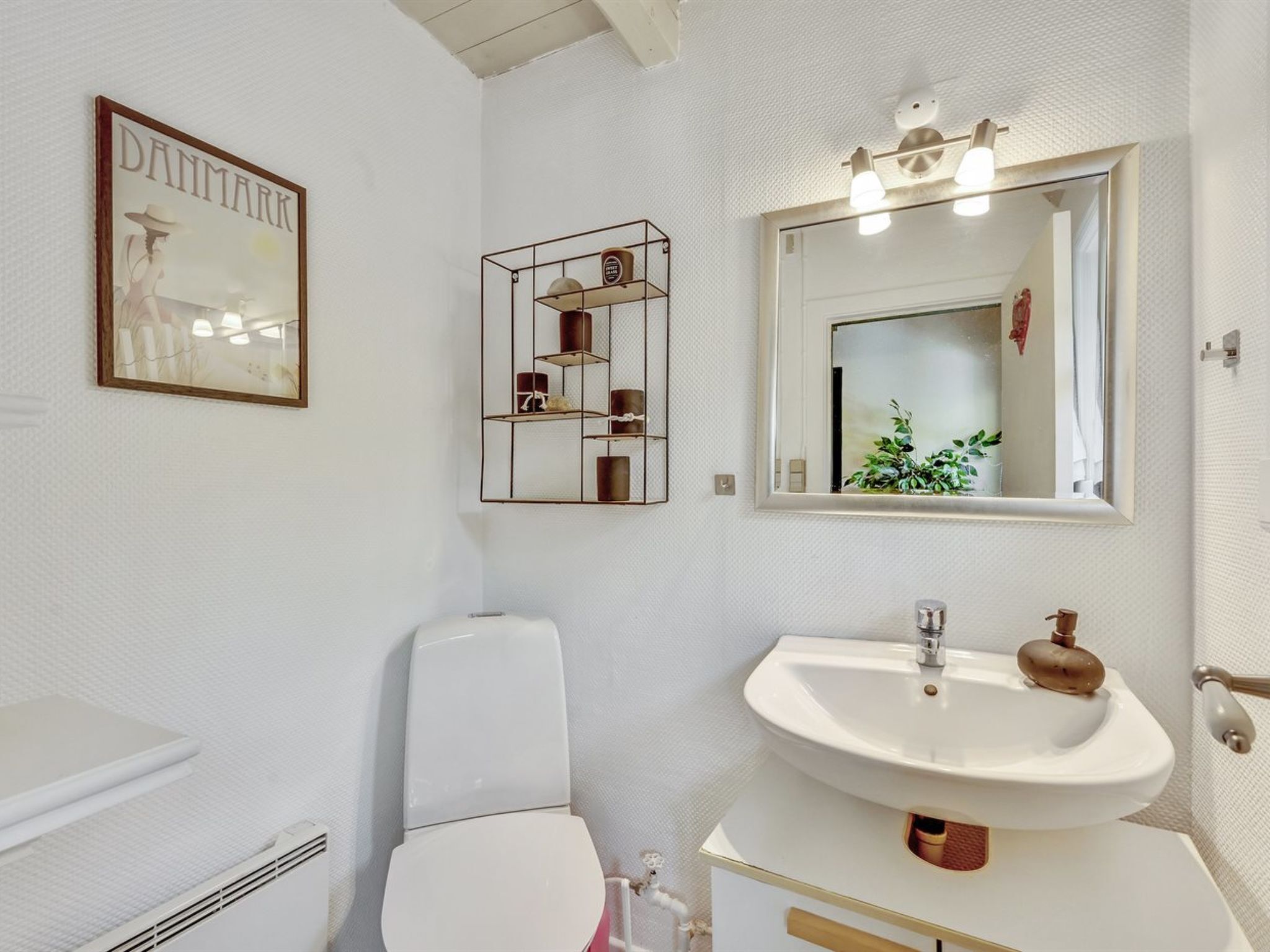 Ein Badezimmer mit Toilette, einem Waschbecken mit Spiegel und einem gerahmten Bild an der Wand.