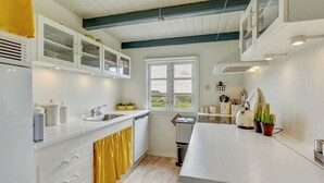 A modern kitchen with white cabinets, a large window, and a yellow curtain.