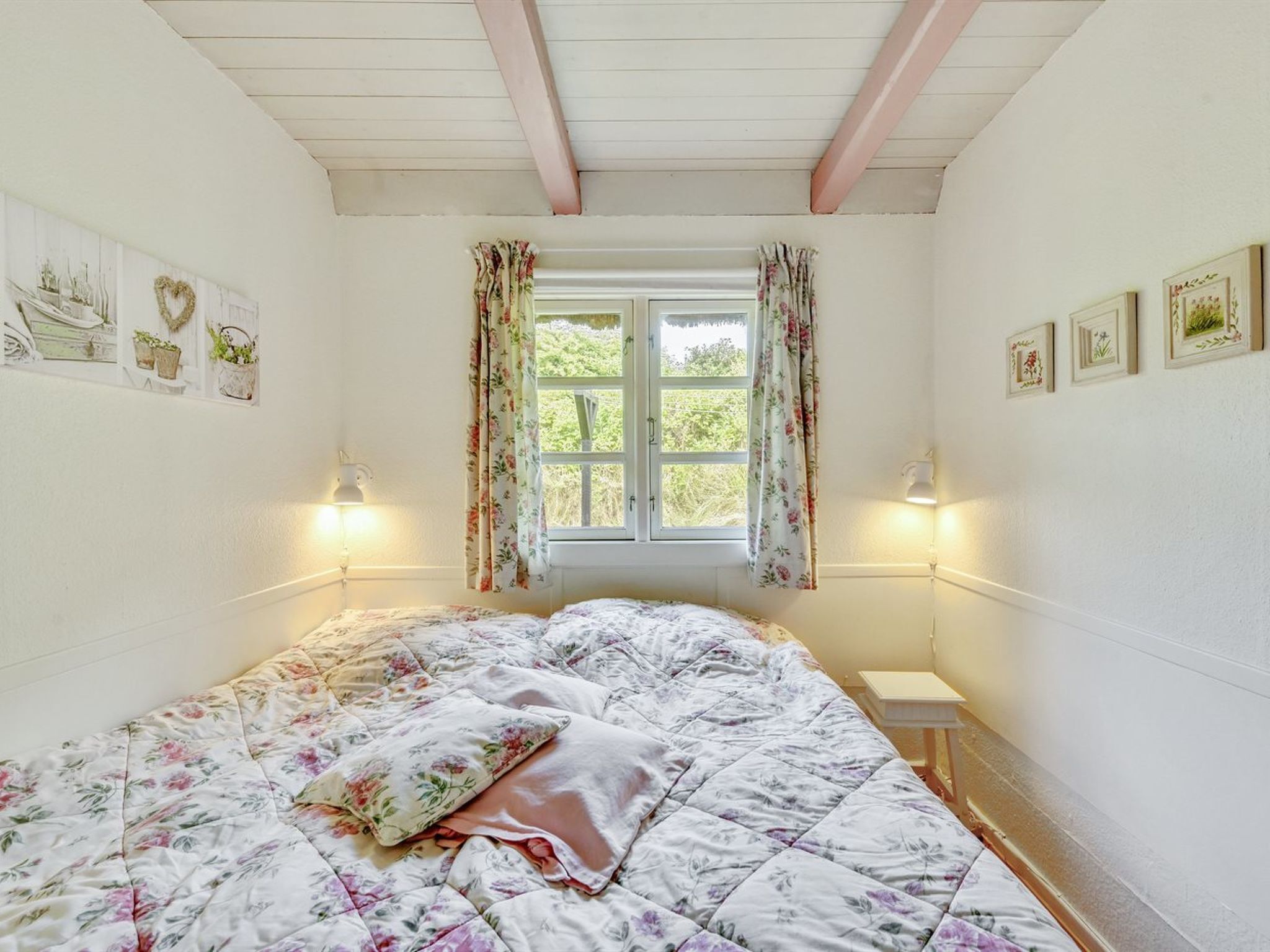 Une chambre avec une couvre-lit à motifs floraux, une fenêtre ornée de rideaux à fleurs et des lampes fixées au mur.