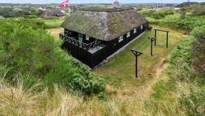 A traditional thatched-roof house with a small porch and a flag, surrounded by greenery.