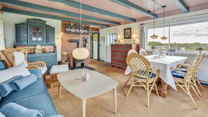 A cozy room with a sofa, a dining table with chairs, a fireplace, and a view through a large window.