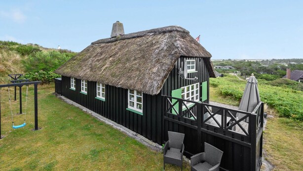 A thatched-roof cottage with a balcony, a swing set, and wicker chairs.