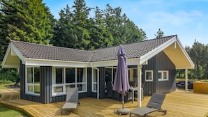 Ein modernes Haus mit überdachter Terrasse, großen Fenstern und einer Holzterrasse.