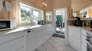 Eine moderne Küche mit Holzwänden, weißen Schränken, einer Mikrowelle, einer Kaffeemaschine und Blick ins Freie.