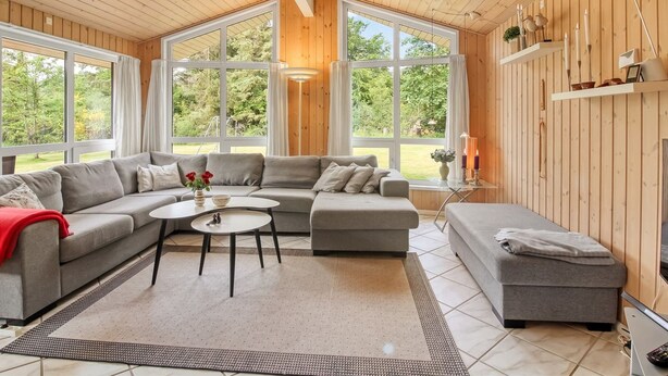 Ein modernes Wohnzimmer mit einem Ecksofa, einem runden Couchtisch und einem kleinen Ottomanen. Große Fenster sorgen für Tageslicht und einen Blick ins Freie.