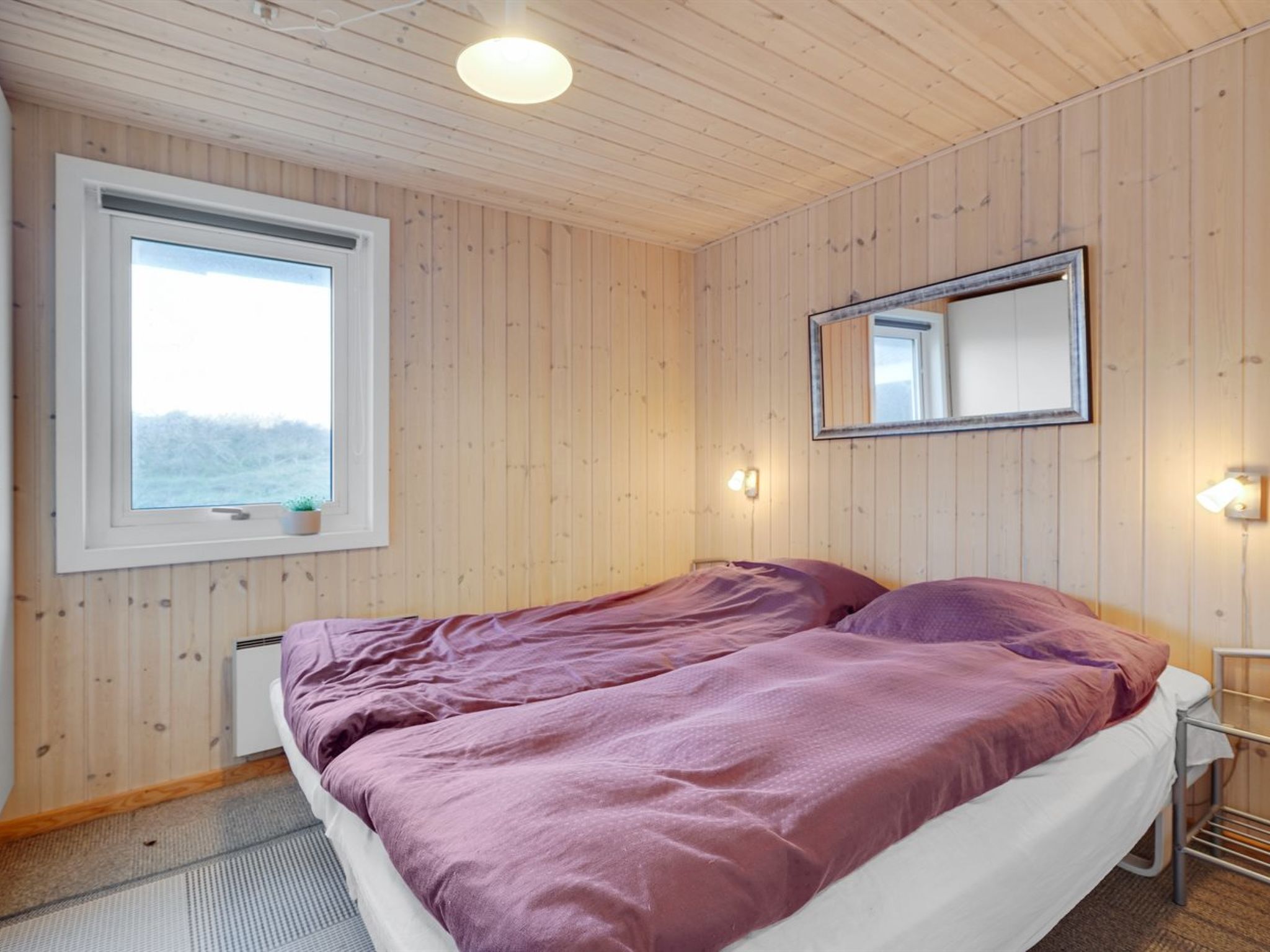 Una camera da letto con un letto, una finestra, uno specchio e un lampadario a parete.