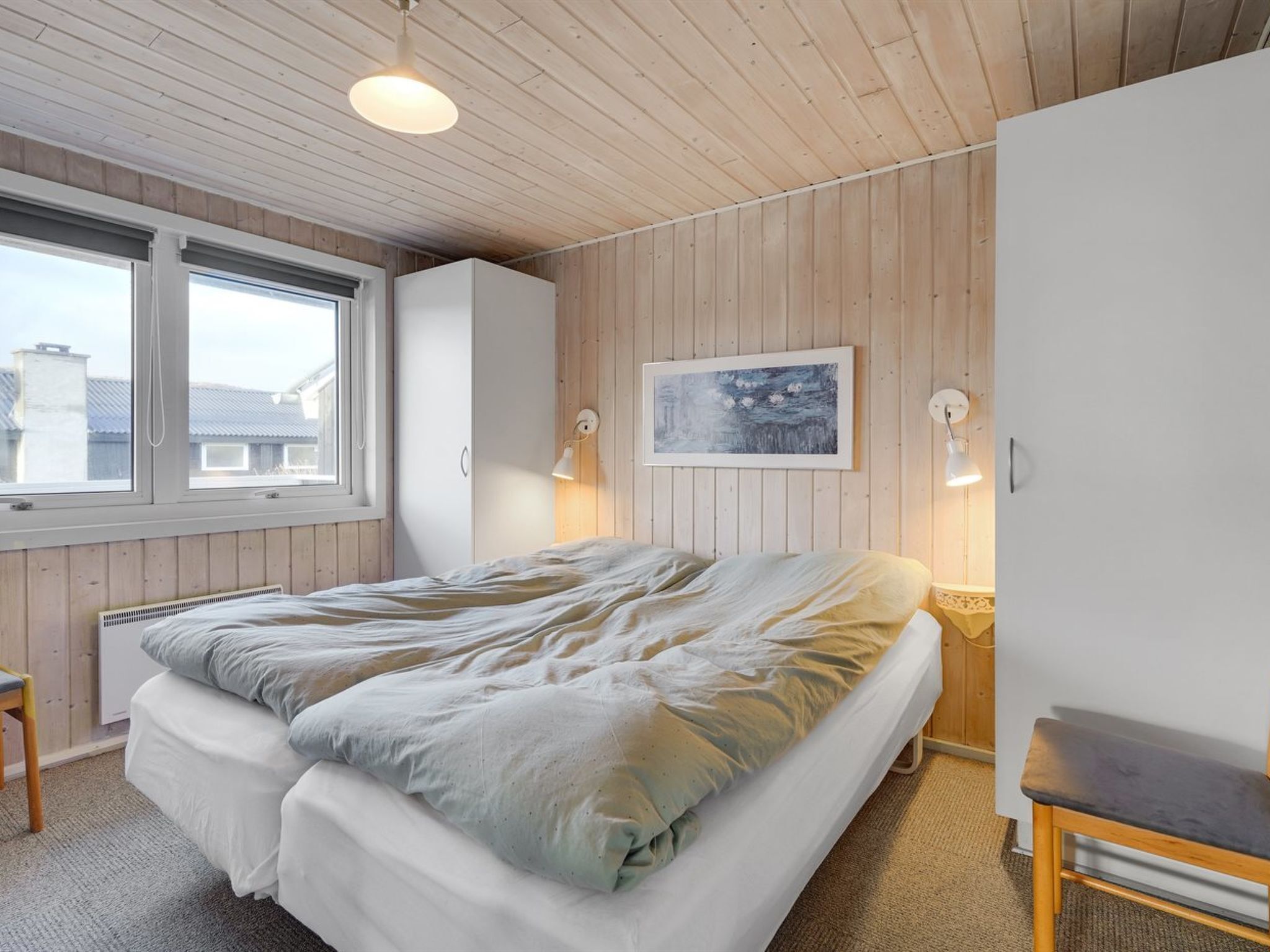 Un dormitorio con cama, ventana, un cuadro y una mesita de noche.