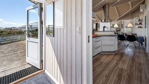 A modern kitchen with wooden paneling, a dining area with black chairs, and a view of the outdoors. - "Sylta" -  from the sea by Interhome (Hvide Sande)