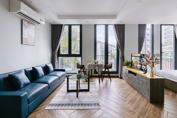 A modern living room with a blue sofa, a glass coffee table, and a dining area with a small table and chairs.