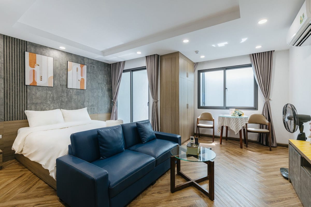 Une chambre d’hôtel moderne avec un lit, un canapé bleu, une petite table à manger et un ventilateur.