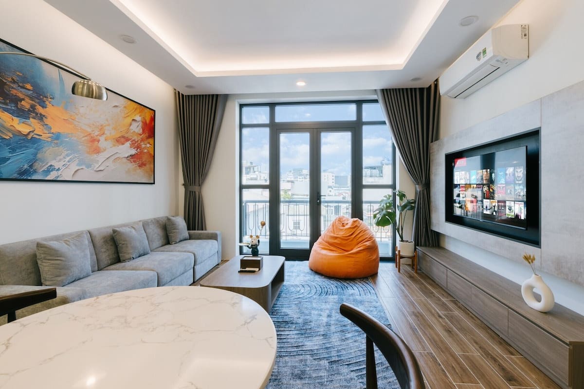 Un salon moderne avec un canapé gris, une table ronde en marbre, un fauteuil poire et un grand téléviseur fixé au mur.
