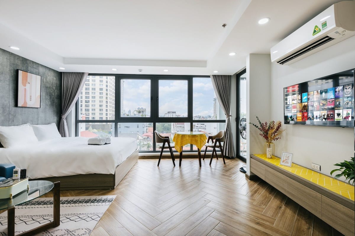 Une chambre d’hôtel moderne avec un grand lit, une petite table à manger, une télévision et une vue sur la ville grâce à de grandes fenêtres.