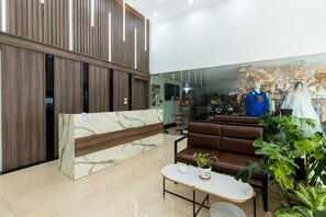 A modern reception area with a marble reception desk, wooden panel walls, a brown leather sofa, and a glass partition with decorative flowers.