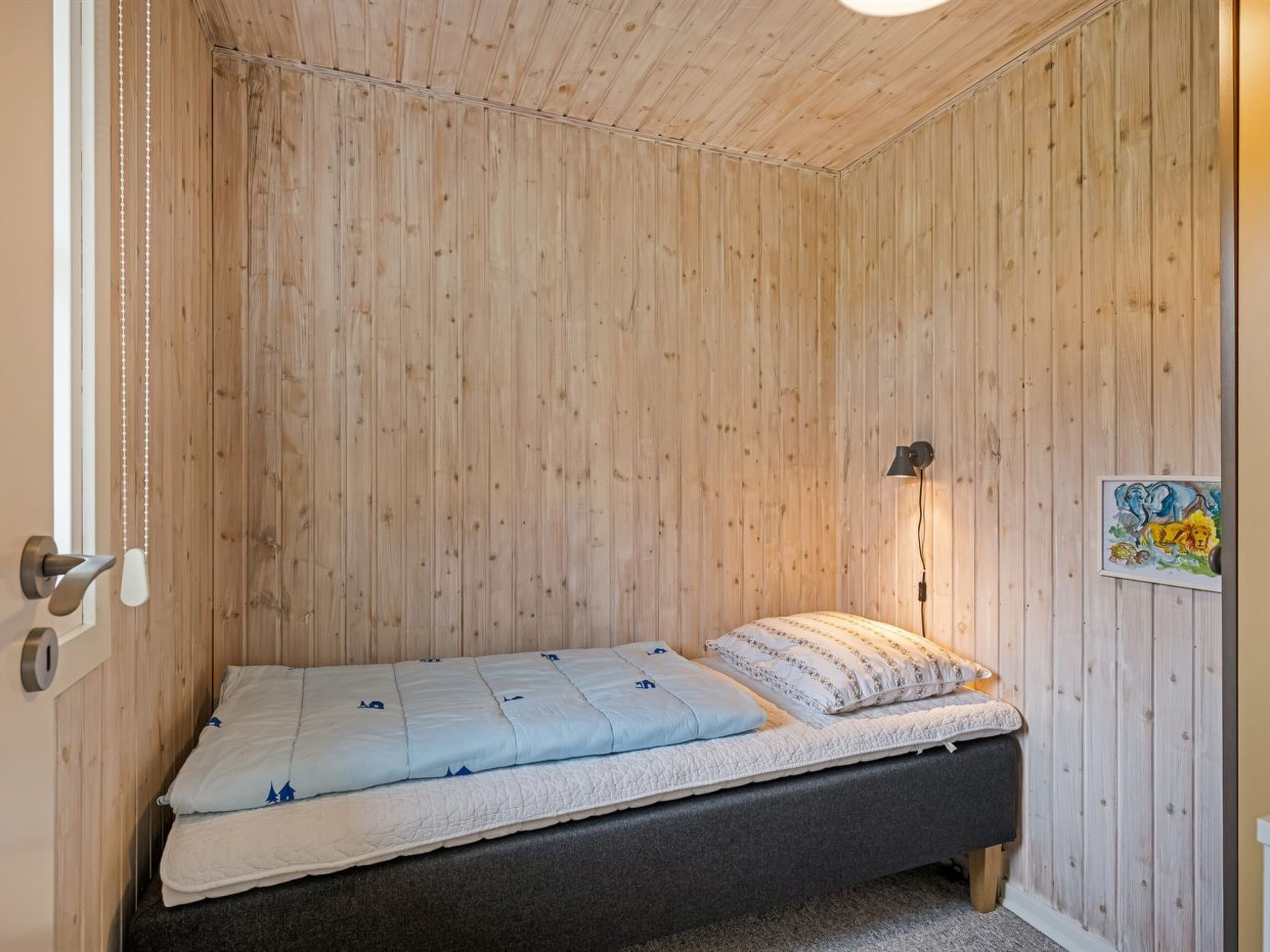 A small, single-bed room with wooden walls and a sloped ceiling.