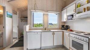 Moderni keittiö, jossa on valkoiset kaapit, sisäänrakennettu uuni ja ikkuna, josta avautuu näkymä vehreään maisemaan.