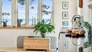 A kitchen with a view of the sea, a wooden bench, a sink, and various kitchen items.