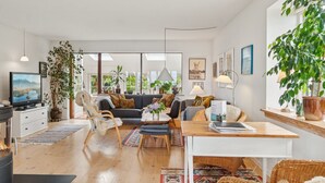 A modern living room with a fireplace, sofa, dining table, and large windows.
