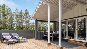 Ein überdachter Außenbereich mit Holzterrasse, Liegestühlen und einem Esstisch.