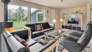 Ein modernes Wohnzimmer mit einem schwarzen Ledersofa, einem Glastisch und einem Fernseher auf einem weißen Schrank.