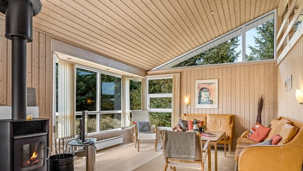 Ein gemütliches Wohnzimmer mit Kamin, Holzböden und großen Fenstern mit Blick auf Grünflächen.