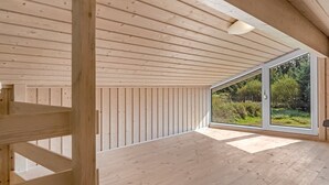 Ein geräumiges Zimmer mit Holzböden und -wänden, große Fenster mit Blick auf grüne Natur.