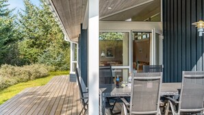 Eine Holzterrasse mit Gartenmöbeln, eine Glastür zu einem Innenbereich und Blick ins Grüne.