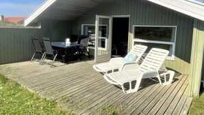 A covered outdoor area with a table and chairs, a deck, and two lounge chairs. - "Juha" -  from the sea by Interhome (Hvide Sande)