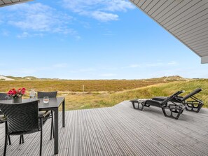 A wooden deck with a table and chairs, lounge chairs, and a view of the landscape.