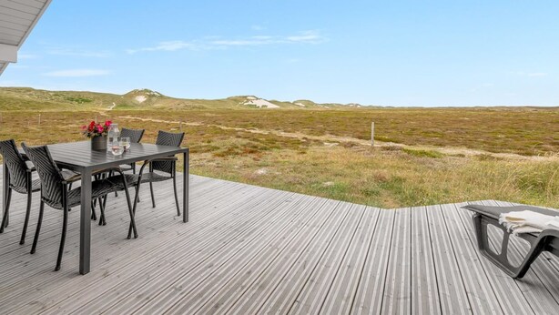 An outdoor deck with a table and chairs, overlooking a grassy landscape with hills.