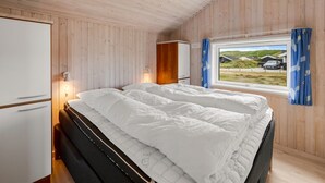 A bedroom with a bed, a wardrobe, a desk, and a window with a view of houses and a car.