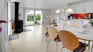 A modern kitchen with white cabinets, a dining area with wooden chairs, and a large window offering a view of greenery.