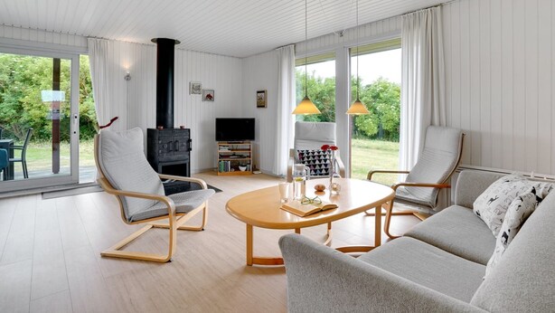 A modern living room with a fireplace, comfortable seating, a television, and large windows offering a view of the outdoors.