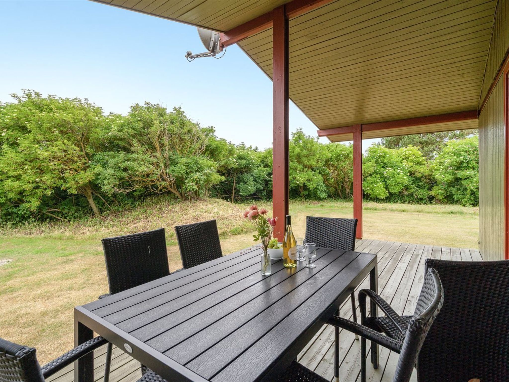Una terraza de madera al aire libre con una mesa y sillas, rodeada de follaje.