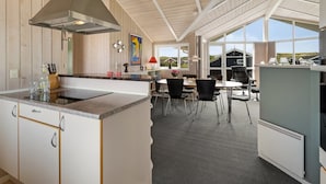 Une cuisine moderne dotée d’un îlot central, de murs recouverts de panneaux en bois et d’une grande fenêtre donnant sur un paysage pittoresque.
