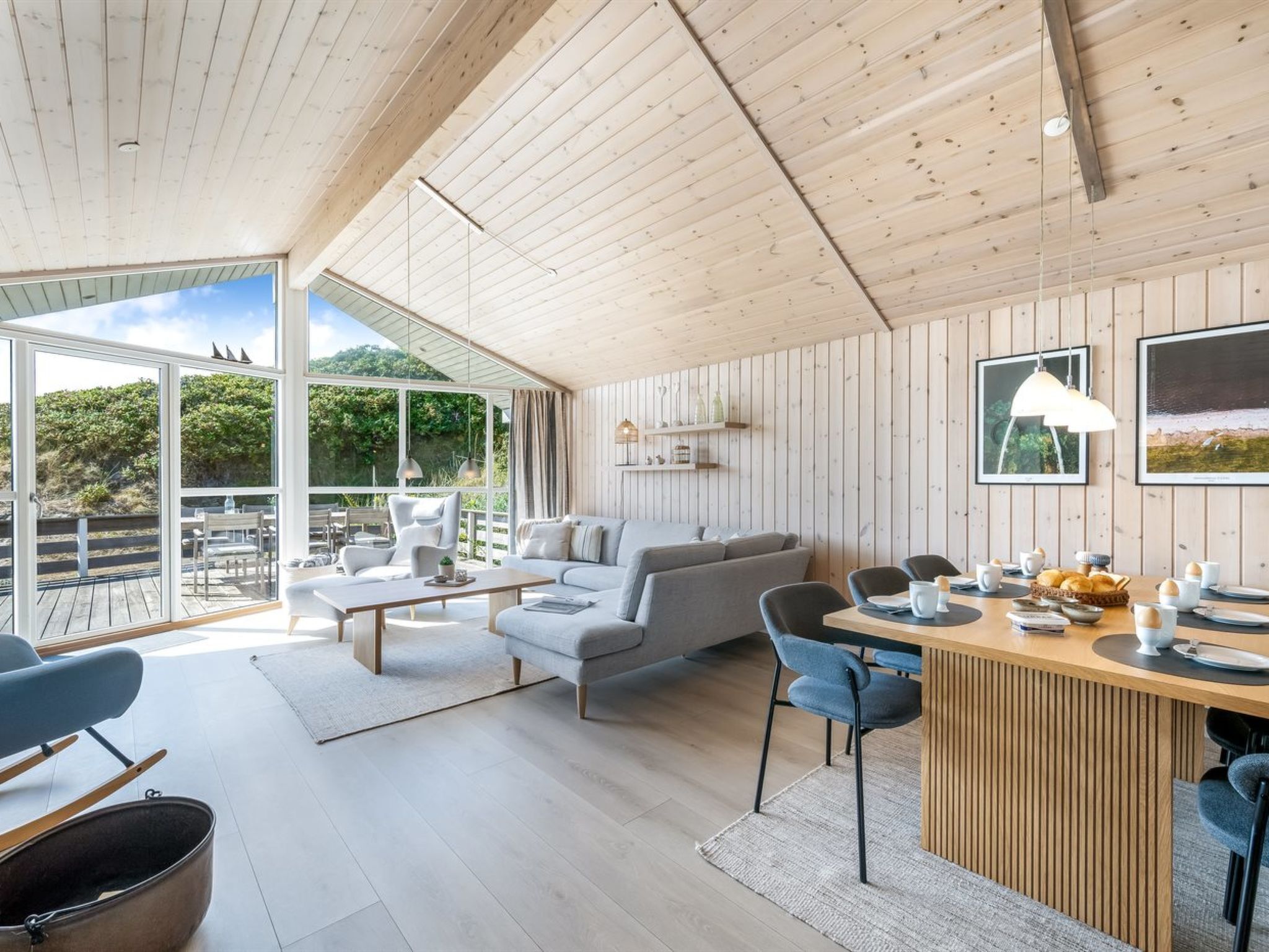 A spacious living area with a wooden ceiling, a large window, and a dining area with a wooden table and chairs.