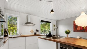 Une cuisine moderne avec des meubles blancs, un plan de travail en bois, un lave-vaisselle encastré et une fenêtre donnant sur un espace verdoyant.