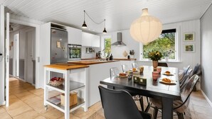 Une cuisine moderne avec des meubles blancs, un îlot central en bois et des luminaires suspendus.