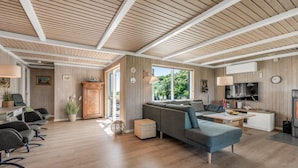 Una sala de estar moderna con techo de madera, un sofá gris, comedor y cocina con televisor.
