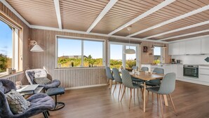 Un comedor amplio con una mesa y sillas de madera, una cocina con armarios blancos y ventanas grandes que ofrecen vista a zonas verdes.